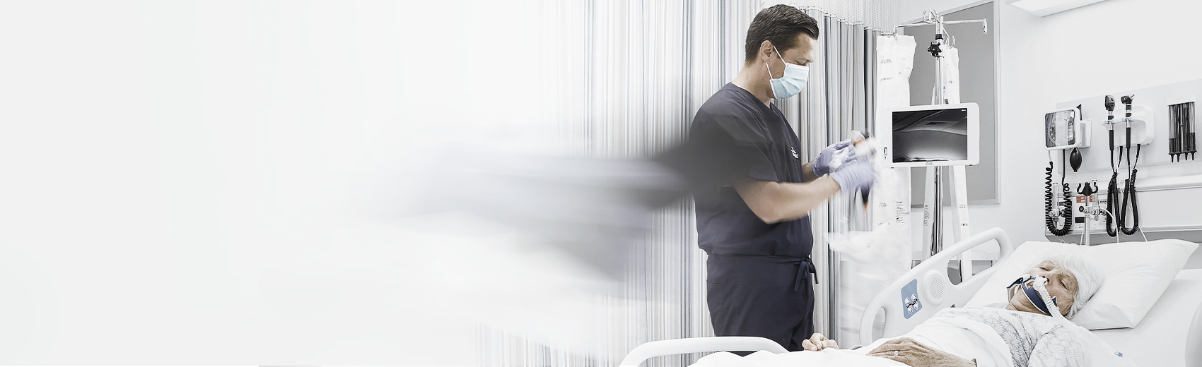 Medical specialist holds device near patient bedside, handling monitors 