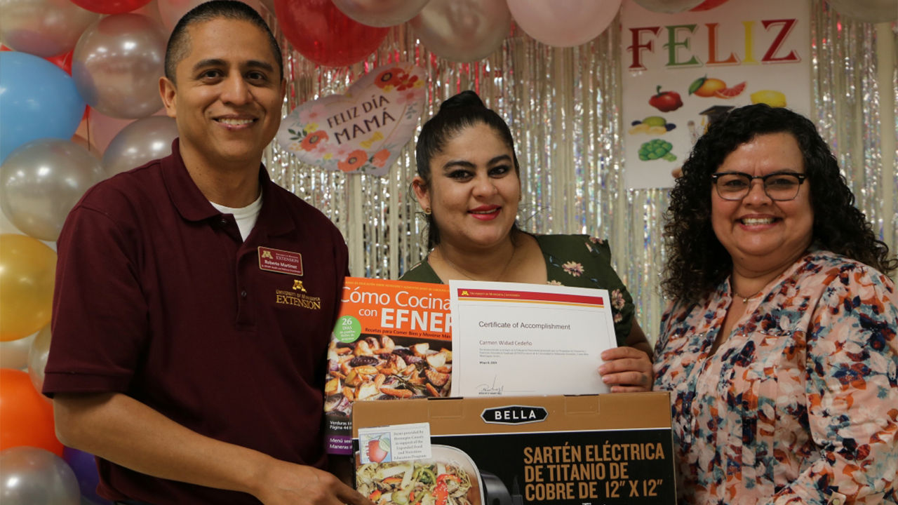 Two smiling woman and a man looking toward camera while holding certificate.